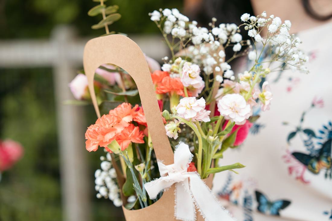 A Sunday Blooms bouquet of peach carnations and stock in a kraft bouquet bag tied with white ribbon