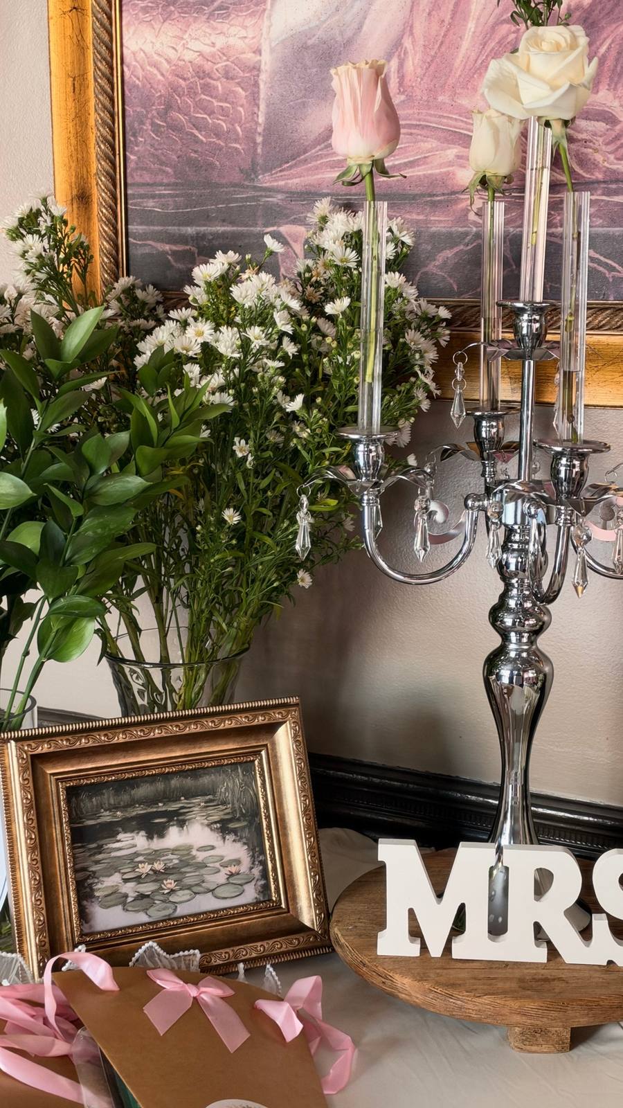 A crystal candelabra holding single roses beside a gold-framed water lily painting