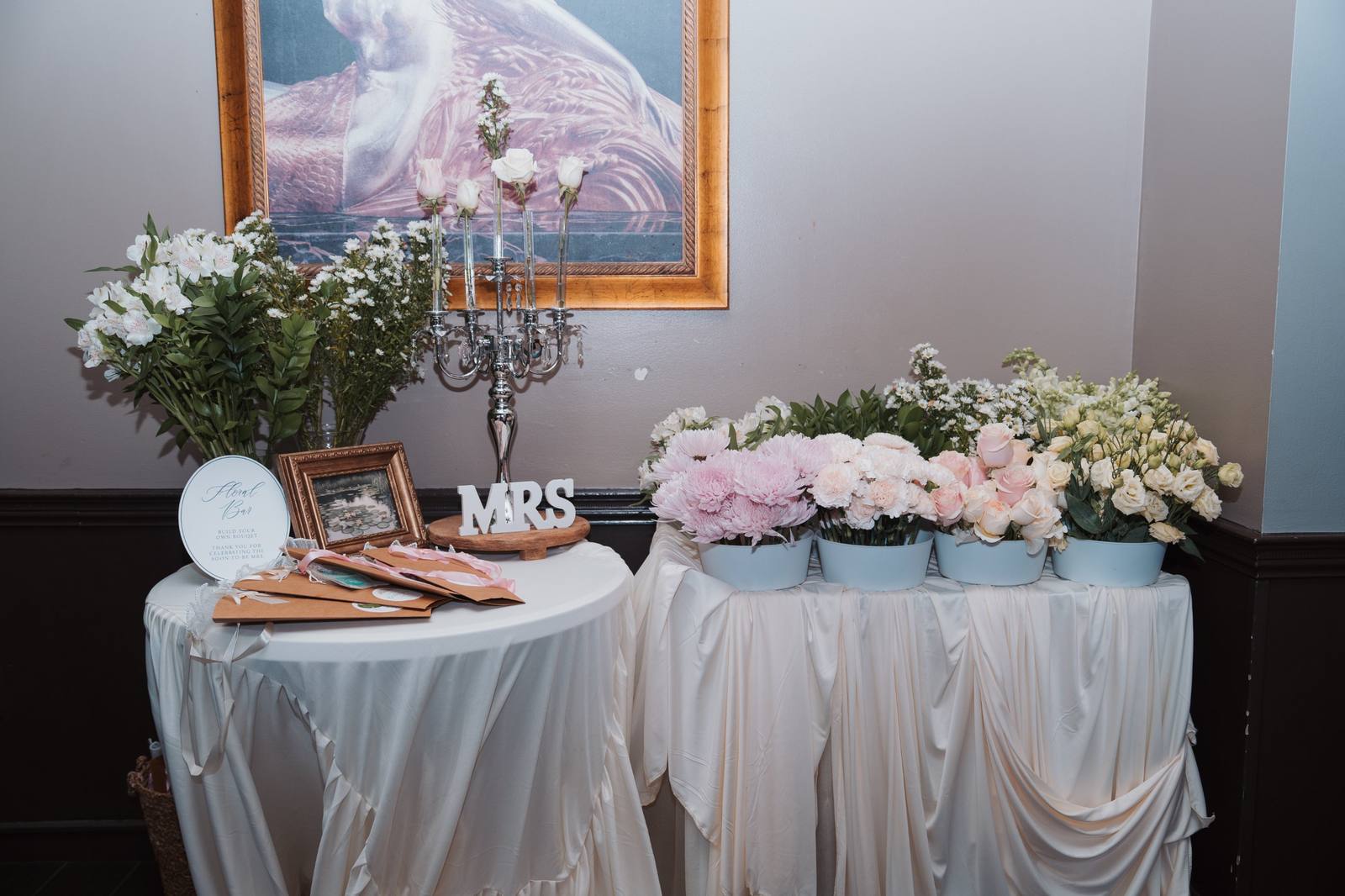 The full bridal shower flower bar: a crystal candelabra, Floral Bar sign, and pots of blush and ivory blooms on draped tables