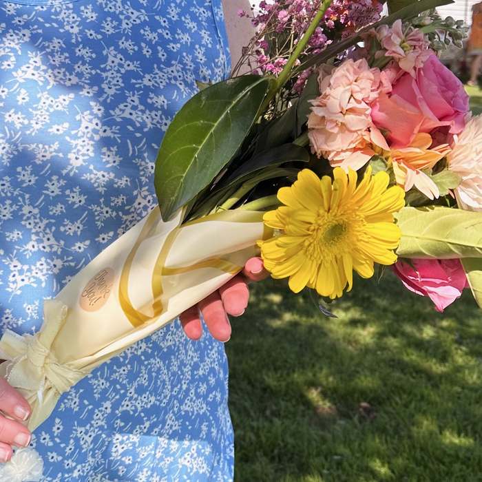 A guest carrying her Sunday Blooms bouquet wrapped with a thank-you sticker