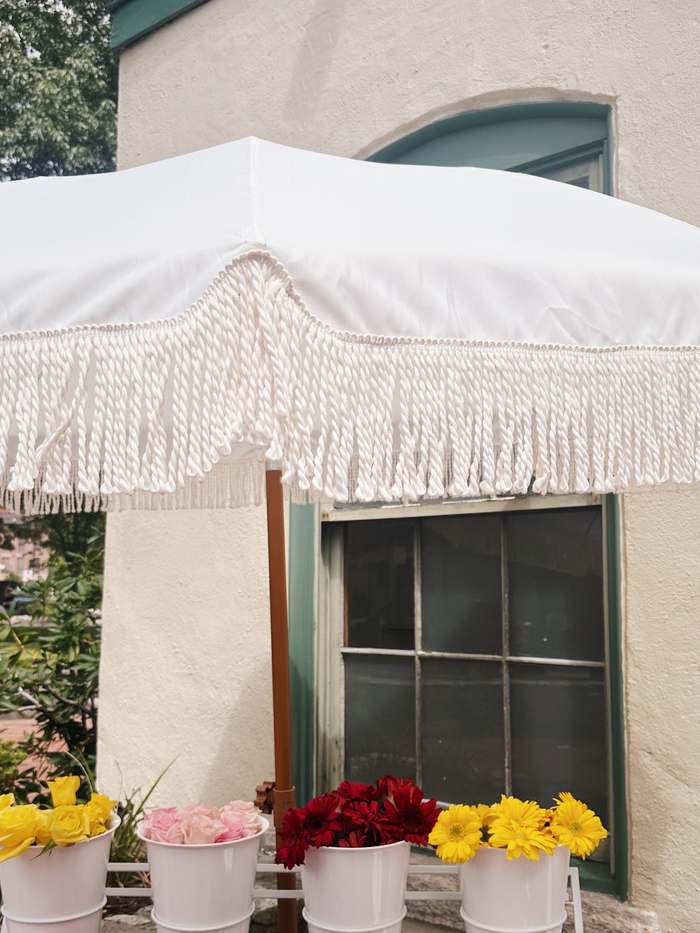 The Sunday Blooms flower bar set up under a white fringe umbrella