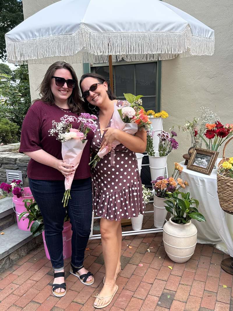 Two smiling guests holding their bouquets under the Sunday Blooms umbrella